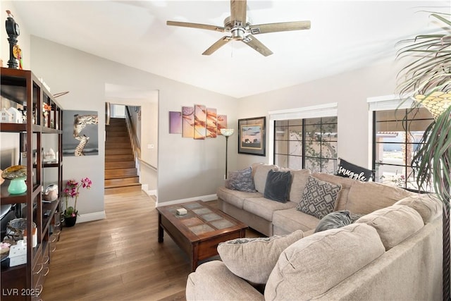 living room with a ceiling fan, baseboards, stairway, and wood finished floors