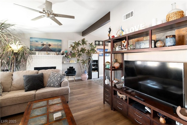 living room featuring lofted ceiling with beams, ceiling fan, wood finished floors, visible vents, and a brick fireplace