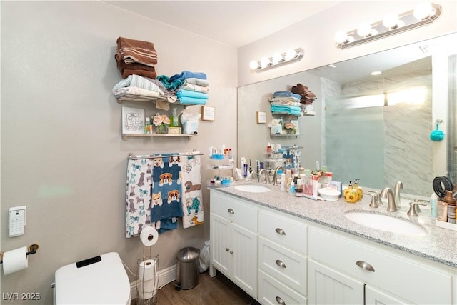 bathroom featuring a shower with shower door, a sink, toilet, and double vanity