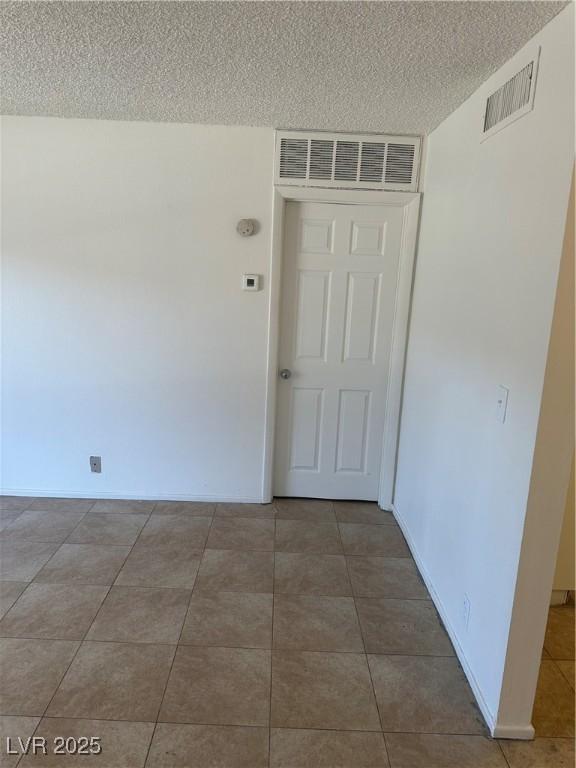 spare room featuring a textured ceiling, baseboards, visible vents, and tile patterned floors