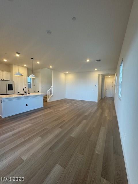 unfurnished living room featuring a sink, stairs, wood finished floors, and recessed lighting