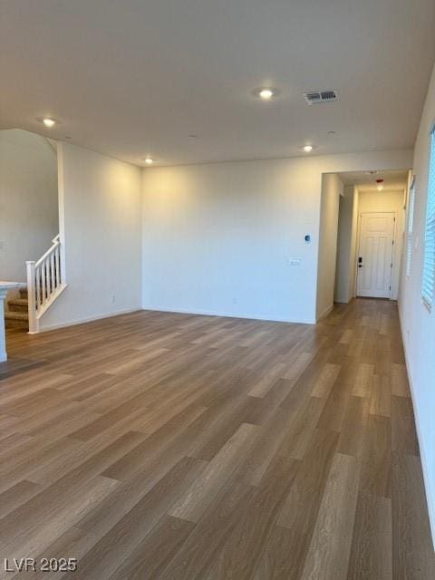 empty room featuring recessed lighting, wood finished floors, visible vents, and stairs