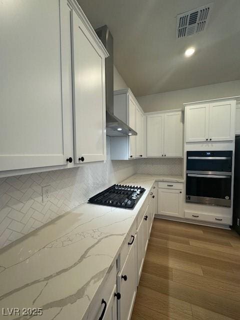 kitchen with visible vents, wall chimney range hood, double oven, white cabinetry, and black gas stovetop