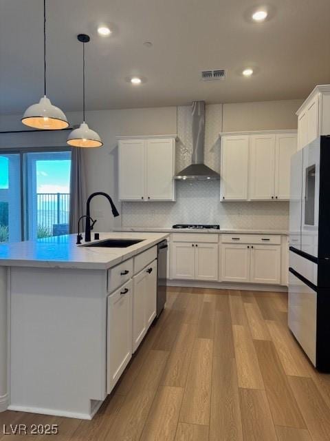 kitchen with dishwasher, wall chimney exhaust hood, stovetop, refrigerator with glass door, and a sink