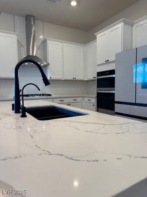 kitchen featuring stainless steel refrigerator, multiple ovens, white cabinets, and light stone counters