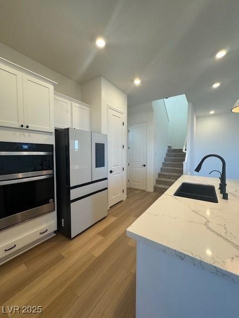 kitchen featuring stainless steel double oven, white cabinets, a sink, wood finished floors, and white refrigerator