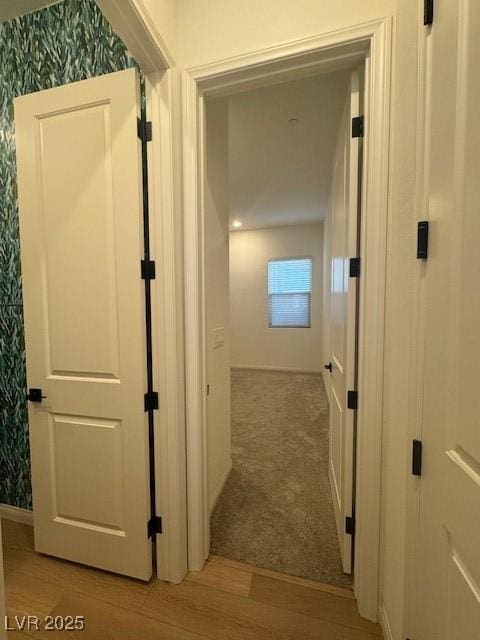 hallway featuring light carpet, light wood-style flooring, and baseboards