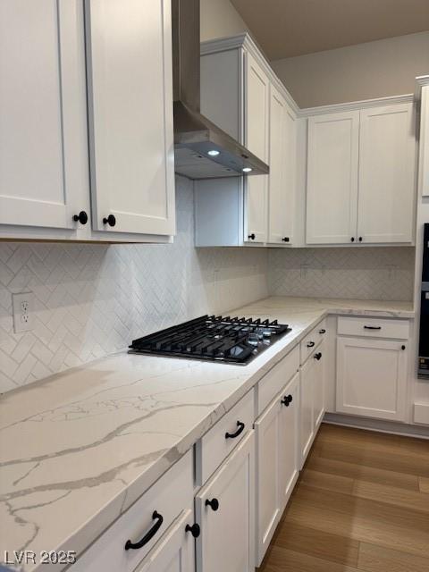 kitchen with stainless steel gas cooktop, backsplash, dark wood-type flooring, white cabinetry, and wall chimney exhaust hood