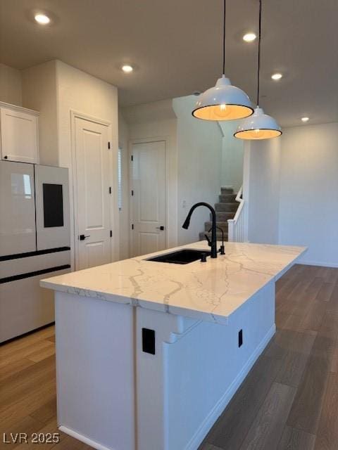 kitchen featuring refrigerator, wood finished floors, a sink, white cabinetry, and light stone countertops