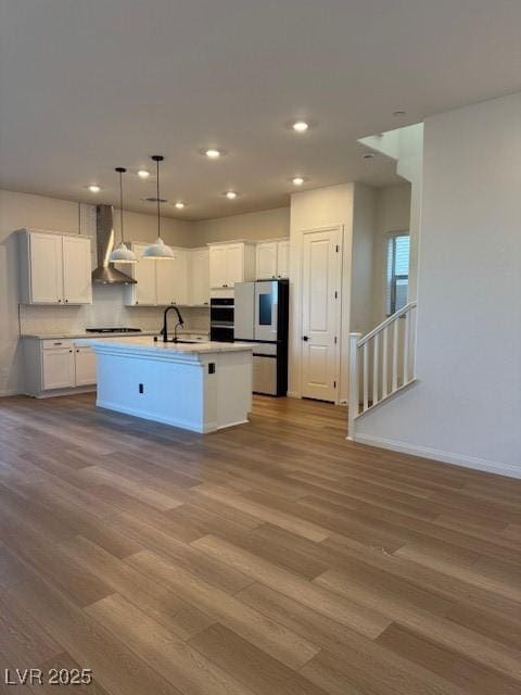 kitchen featuring dark wood-type flooring, white cabinetry, freestanding refrigerator, wall chimney exhaust hood, and a center island with sink