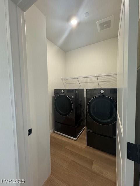 clothes washing area with laundry area, washing machine and dryer, visible vents, and wood finished floors