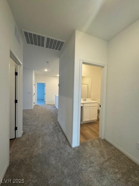 corridor with a sink, baseboards, visible vents, and carpet flooring