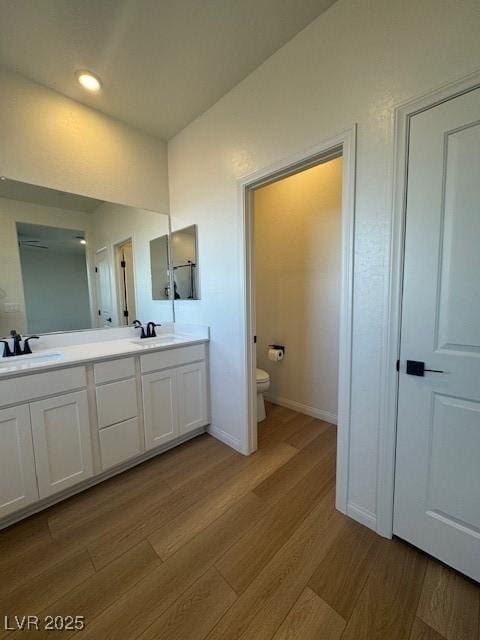 bathroom featuring double vanity, wood finished floors, a sink, and toilet