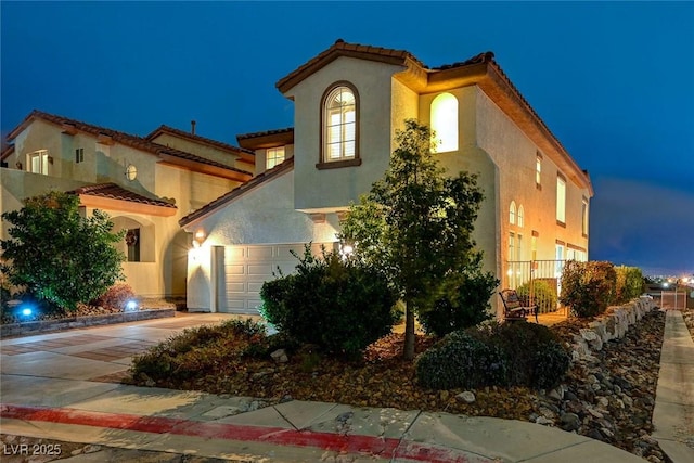 mediterranean / spanish home featuring driveway, a tile roof, a garage, and stucco siding