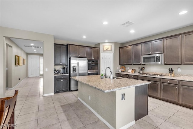 kitchen with light stone counters, appliances with stainless steel finishes, light tile patterned flooring, a sink, and dark brown cabinets