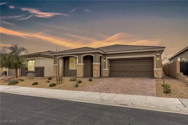 view of front of home featuring a garage, stone siding, fence, decorative driveway, and stucco siding