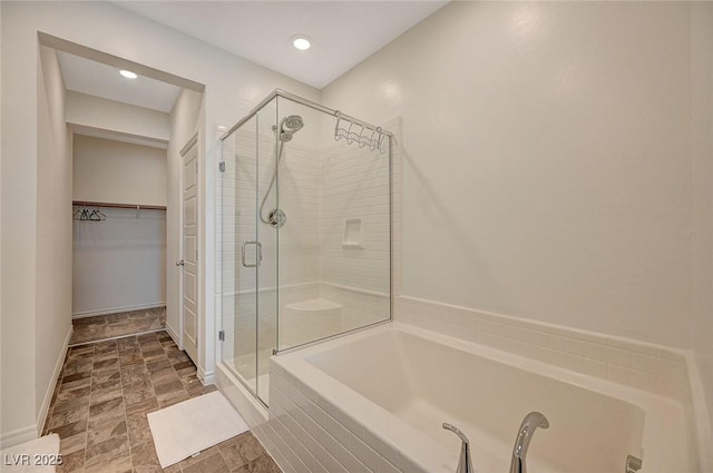 bathroom with a stall shower, a walk in closet, a bath, and baseboards