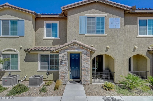 view of front facade featuring stone siding, central air condition unit, and stucco siding