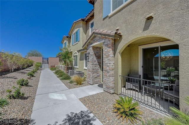 view of side of property with stone siding, a tiled roof, a gate, fence, and stucco siding