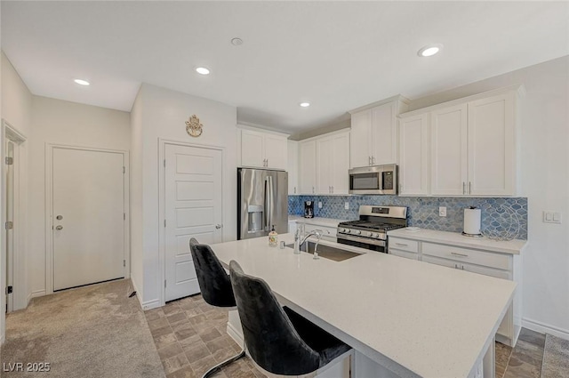 kitchen featuring decorative backsplash, appliances with stainless steel finishes, a kitchen island with sink, light countertops, and a sink