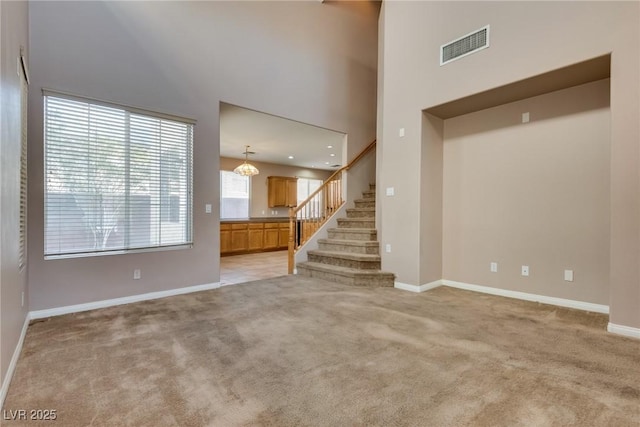 unfurnished living room featuring light colored carpet, a towering ceiling, baseboards, stairs, and visible vents