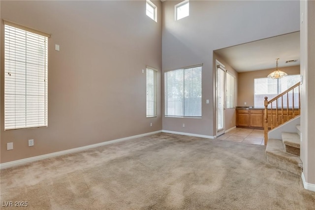 unfurnished living room featuring light carpet, a high ceiling, baseboards, stairway, and an inviting chandelier