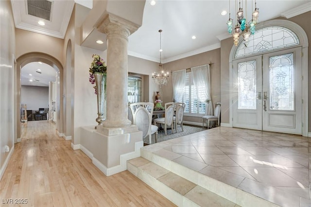 foyer entrance featuring baseboards, visible vents, arched walkways, crown molding, and a notable chandelier