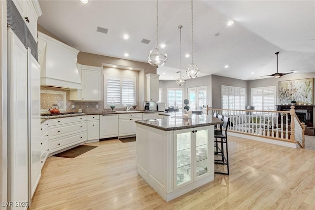 kitchen featuring white cabinets, dishwasher, a kitchen island, premium range hood, and gas stovetop