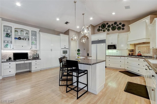 kitchen with built in appliances, premium range hood, visible vents, built in study area, and a kitchen bar