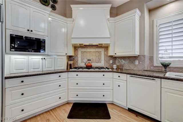 kitchen with premium range hood, black microwave, white cabinets, and gas cooktop