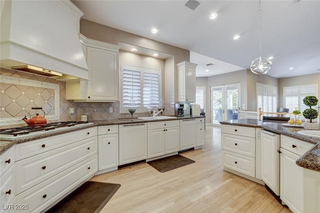 kitchen featuring white appliances, light wood finished floors, white cabinets, premium range hood, and a sink