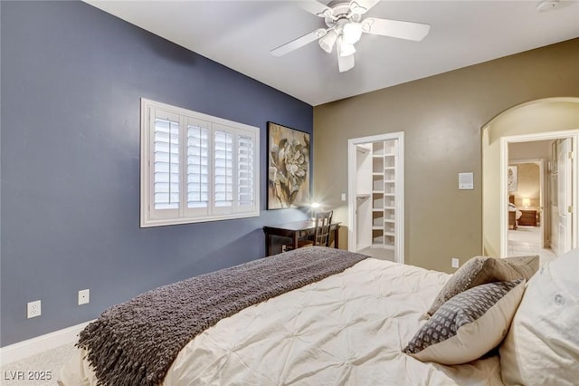 bedroom featuring arched walkways, a walk in closet, carpet, a ceiling fan, and baseboards