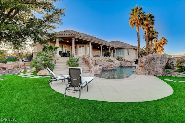 back of house with a tile roof, a patio area, a lawn, and stucco siding