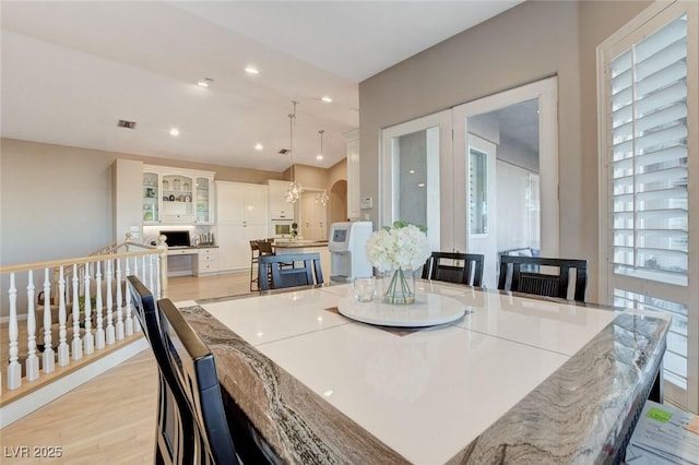 dining space with light wood-style flooring, visible vents, arched walkways, and recessed lighting