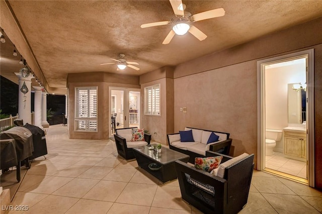 living area with a ceiling fan, light tile patterned flooring, and ornate columns