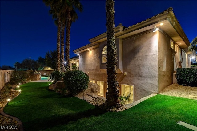 property exterior at twilight with a tile roof, fence, a lawn, and stucco siding