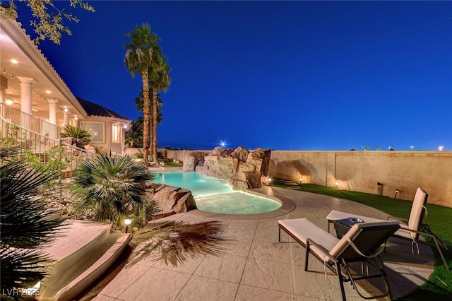 pool at night featuring a fenced in pool, a patio, a jacuzzi, and fence