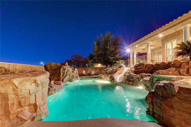 pool at night with french doors, a water slide, and a fenced in pool