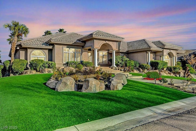 mediterranean / spanish-style house featuring a front yard, a tile roof, and stucco siding