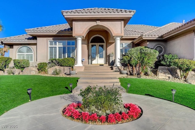 view of exterior entry featuring a tiled roof, french doors, a lawn, and stucco siding