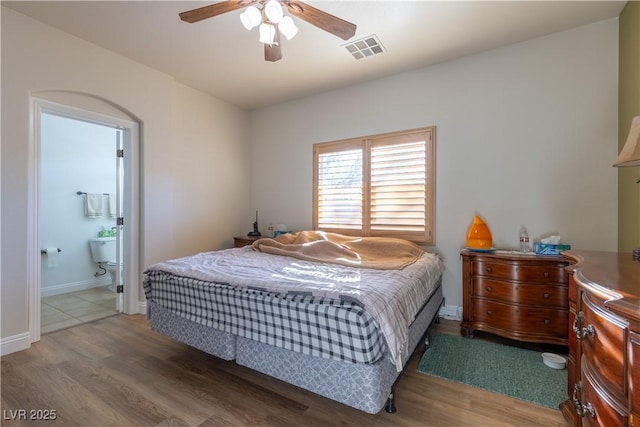 bedroom with baseboards, visible vents, connected bathroom, ceiling fan, and wood finished floors