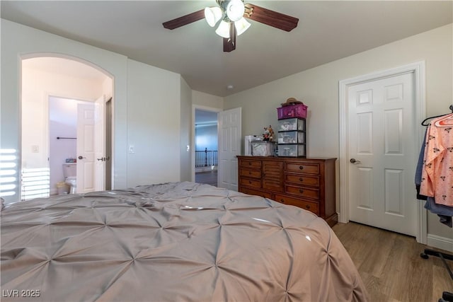 bedroom featuring arched walkways, wood finished floors, a ceiling fan, and ensuite bathroom