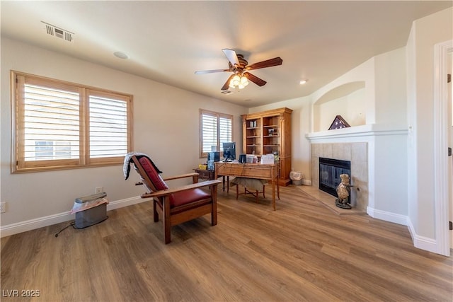 office area featuring wood finished floors, a tile fireplace, visible vents, and baseboards