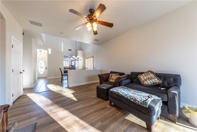 living area with baseboards, visible vents, wood finished floors, vaulted ceiling, and ceiling fan with notable chandelier