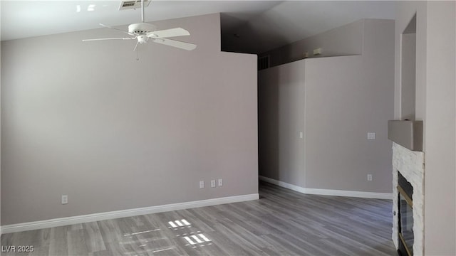 unfurnished living room featuring a stone fireplace, wood finished floors, baseboards, and ceiling fan