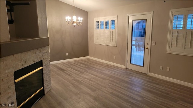 unfurnished living room with wood finished floors, a stone fireplace, baseboards, a chandelier, and vaulted ceiling