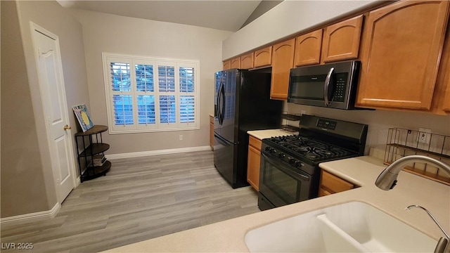 kitchen with brown cabinetry, lofted ceiling, a sink, black appliances, and light countertops