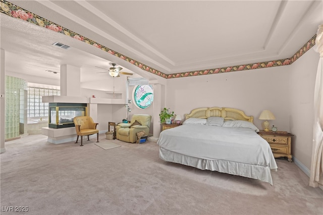 bedroom featuring ceiling fan, carpet flooring, a multi sided fireplace, visible vents, and a raised ceiling