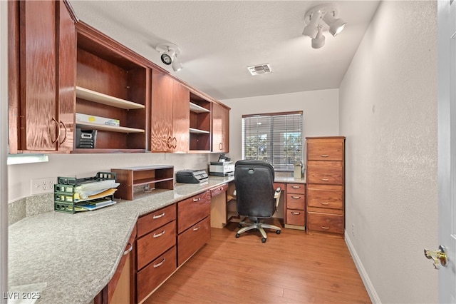 office area with baseboards, visible vents, a textured ceiling, light wood-style floors, and built in desk