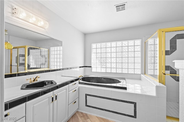 full bathroom featuring visible vents, wood finished floors, a garden tub, a tile shower, and vanity